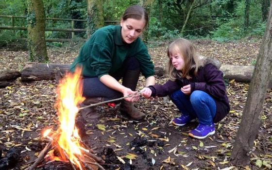 A member of staff and child toasting marshmallows on a fire in the woods