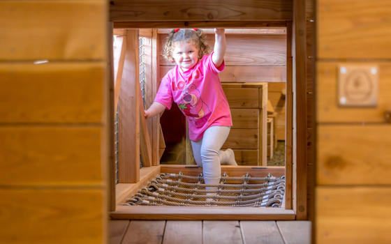 Young girl wearing a pink t-shirt having fun on the wooden indoor adventure play equipment